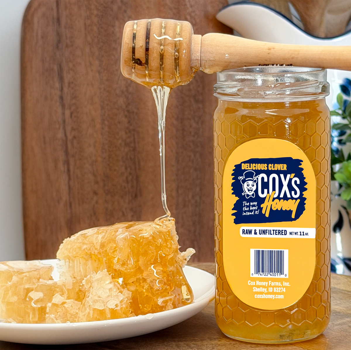 Coxs Honey 11 oz glass jar with honey dripping from a honey dipper onto honeycomb sitting on a wood chopping block