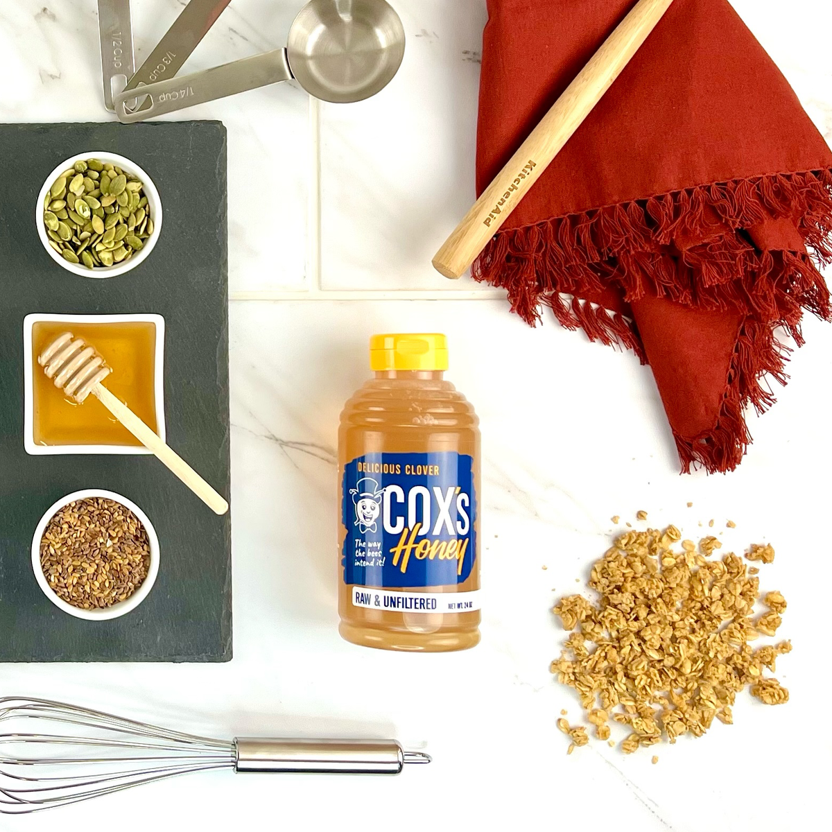 Coxs honey bottle with ingredients and utensils on a white surface