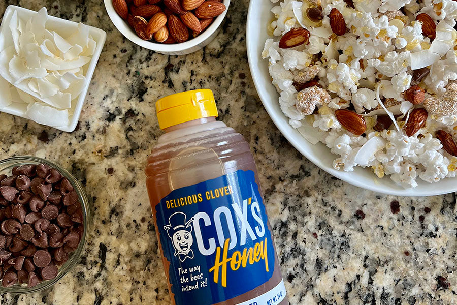 Cox's Honey Flavor your Popcorn with Honey. Popcorn with Cox's clover honey bottle. Honey drizzled on the popcorn with almonds and coconut