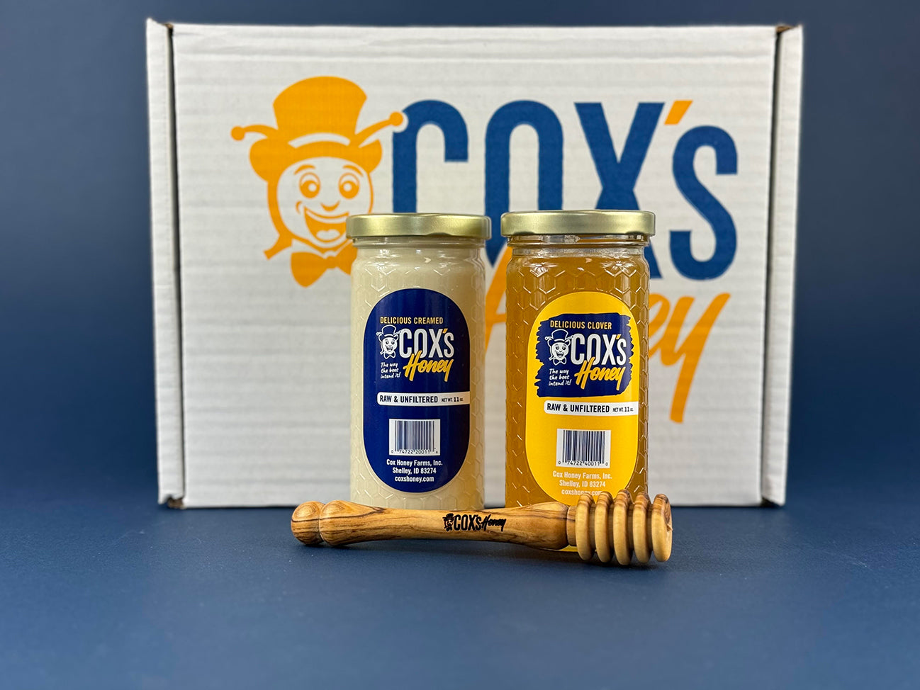 Cox's Honey Gift Set with 1 - 11 oz clover honey glass jar and 1 - 11 oz creamed honey glass jar and 1 olive wood honey dipper on outside of box