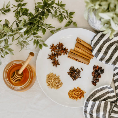 elderberry syrup kit spices and herbs on a white plate with a honey dipper and striped towel.