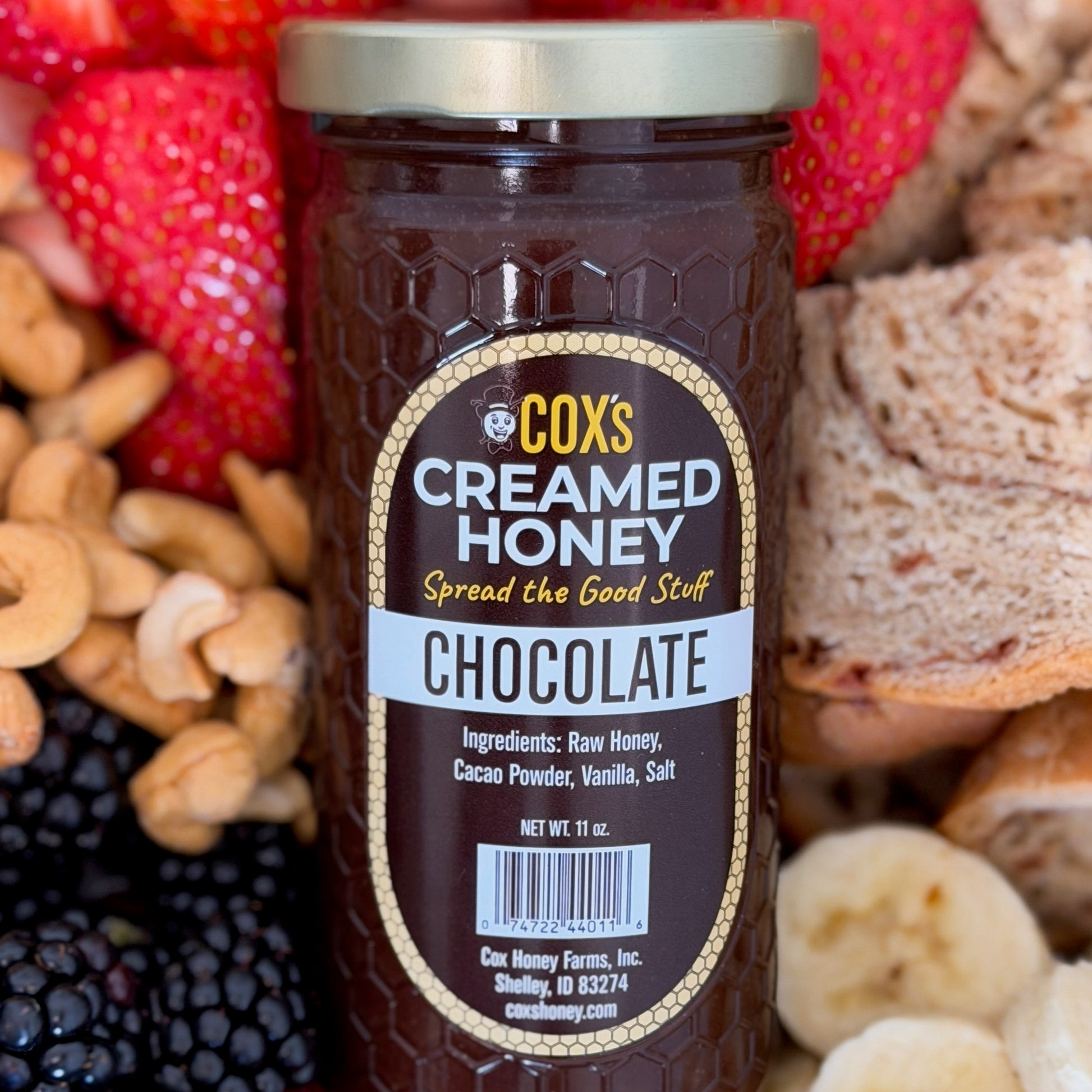 Jar of Cox's Creamed Honey Chocolate surrounded by snacks like strawberries, nuts, and bread.