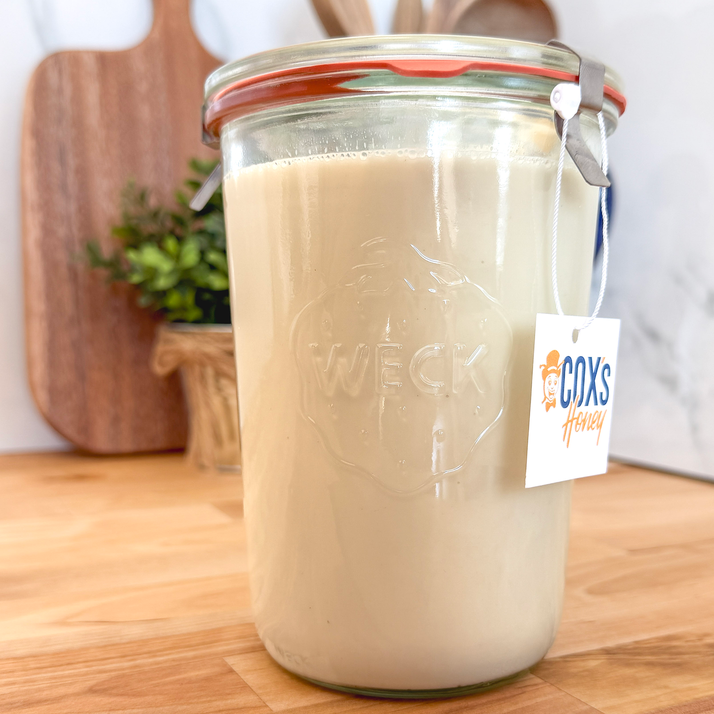 Weck Glass jar filled with creamed honey, on a wooden surface with a Coxs Honey tag.