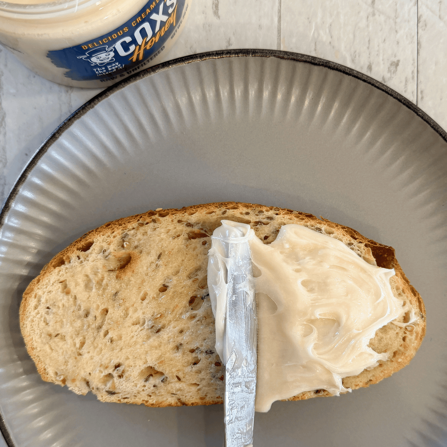 Bread with creamed honey spread on a metal plate, next to a jar of creamed honey.