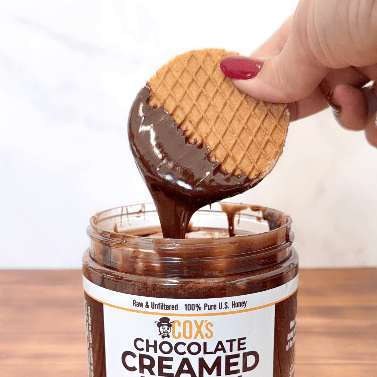 Coxs Honey 20 oz Chocolate Creamed Honey with a waffle dipped into the chocolate honey and pulling it out