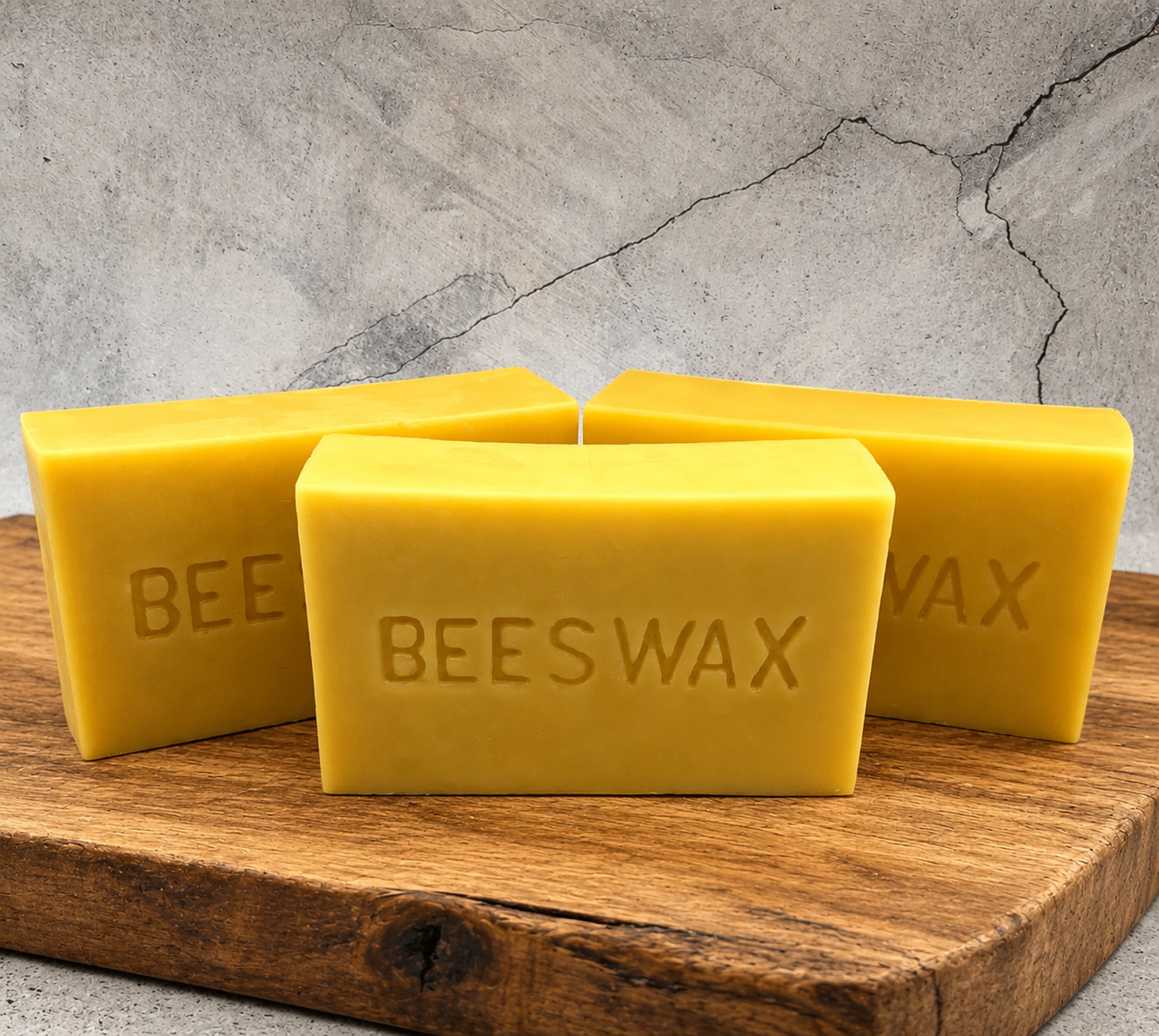 Three bars of beeswax on a wooden cutting board with a concrete wall background.