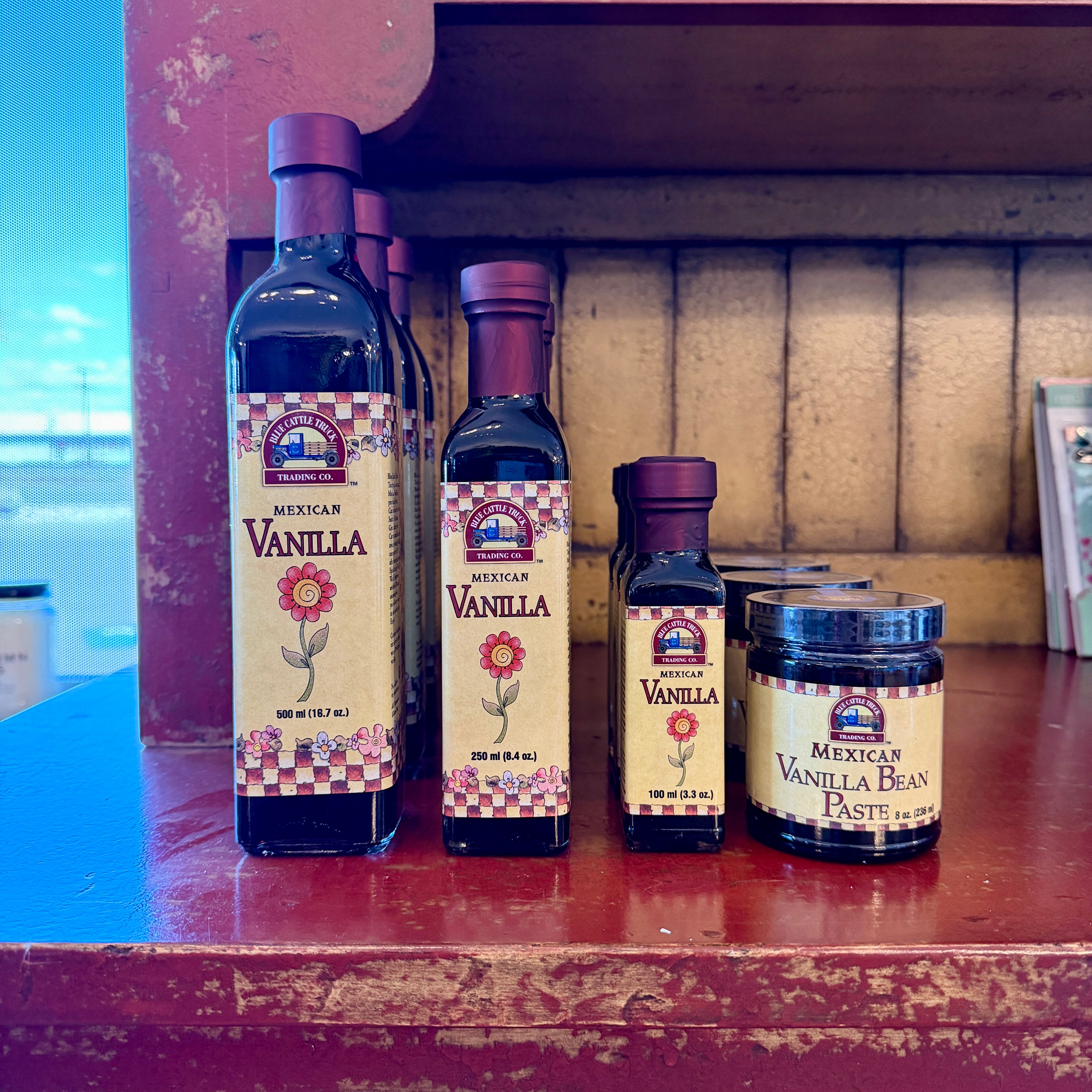 Bottles and a jar of vanilla products on a wooden shelf.