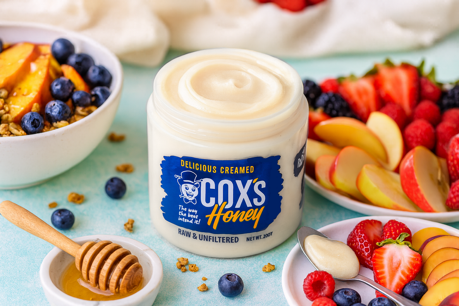 Jar of Cox's Honey surrounded by fruit and honey on a light blue background