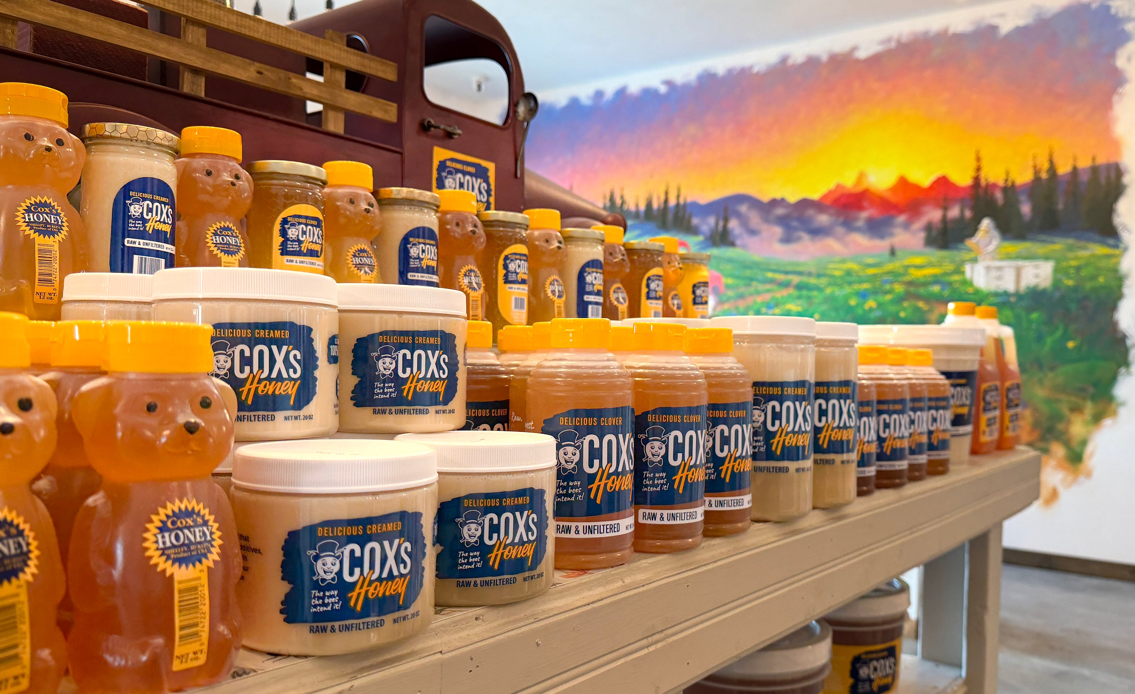 Row of Cox's Honey jars on a shelf with a scenic background