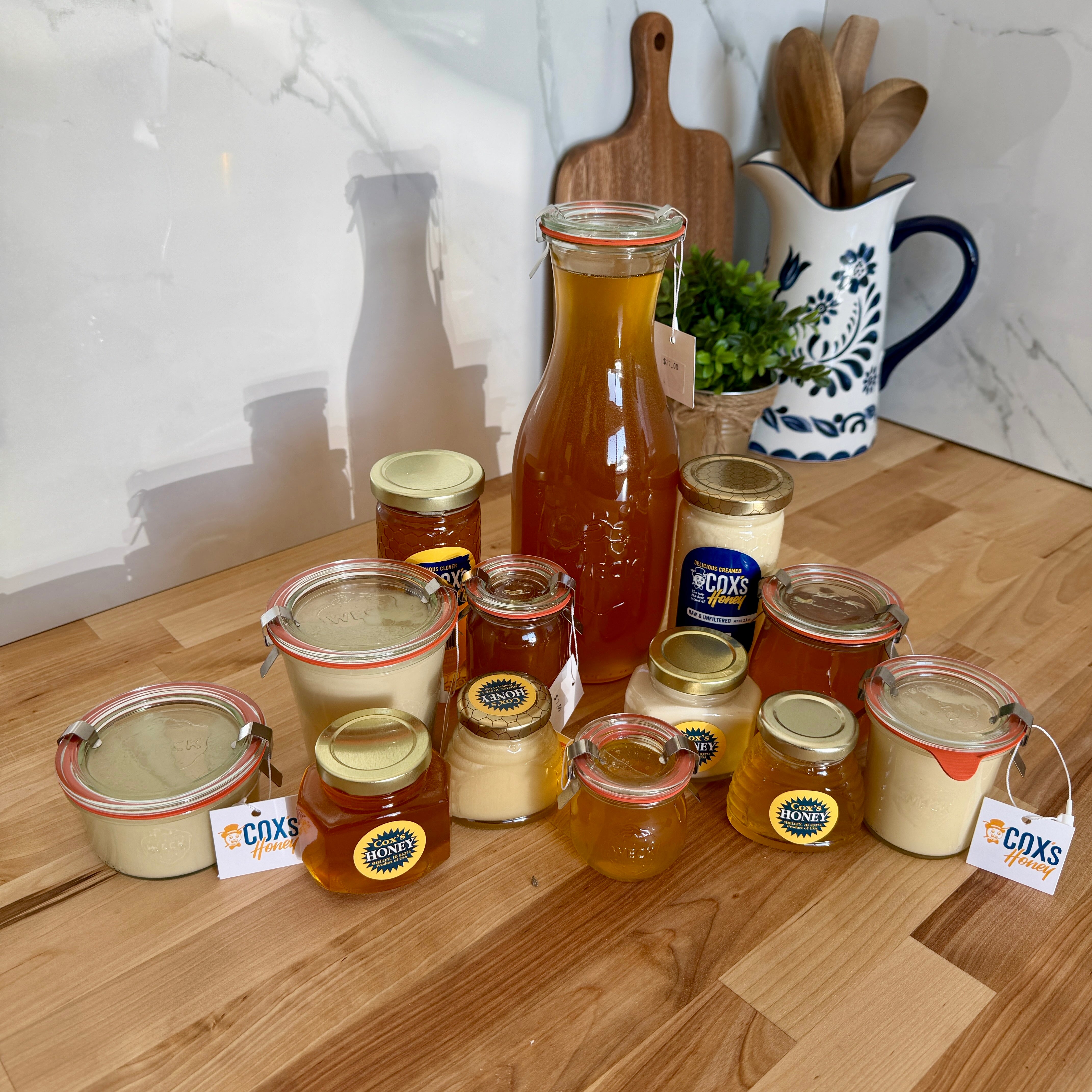 Assorted jars and bottles of honey on a wooden surface with a white marble wall in the background.