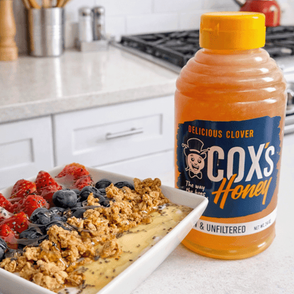 Bottle of Cox's Honey on a kitchen counter with a dish of granola and fruit.