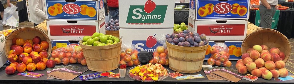 Display of fresh fruits including apples, oranges, and peaches with Symms and SSS Fruit boxes in the background.